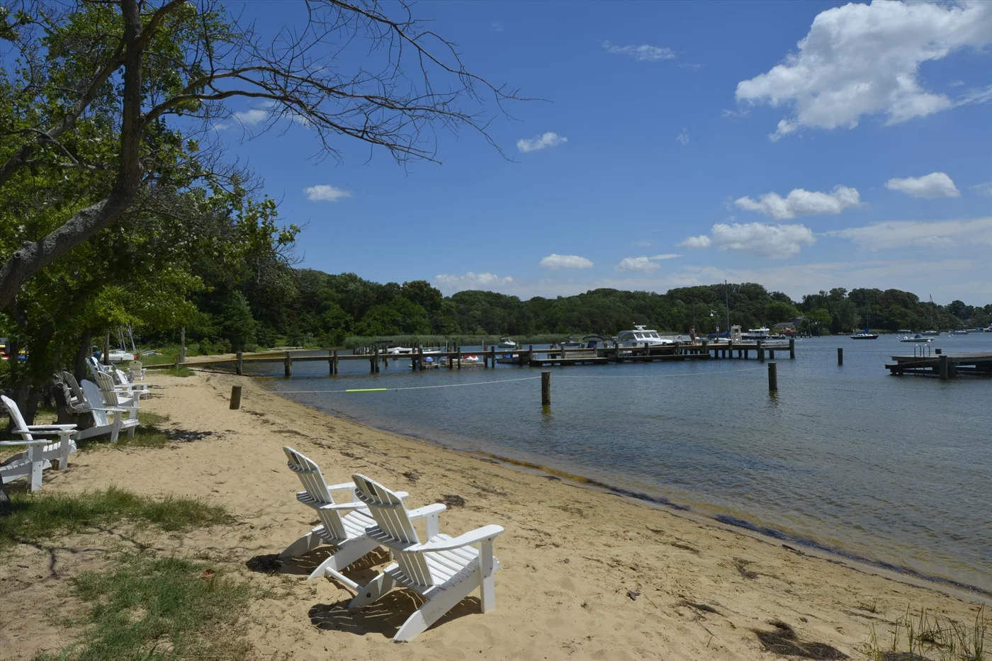 White Adirondack chairs on Olde Severna Park’s sandy community beach with piers beyond